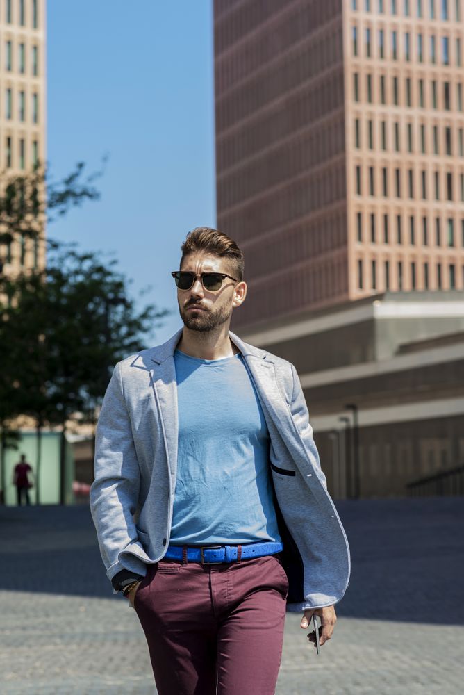 Man with sunglasses walking with hand on pocket outside on sunny day