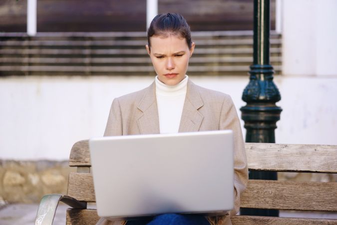 A Focused Woman Concentrating While Working on Her Laptop Outdoors in a Vibrant Urban Setting