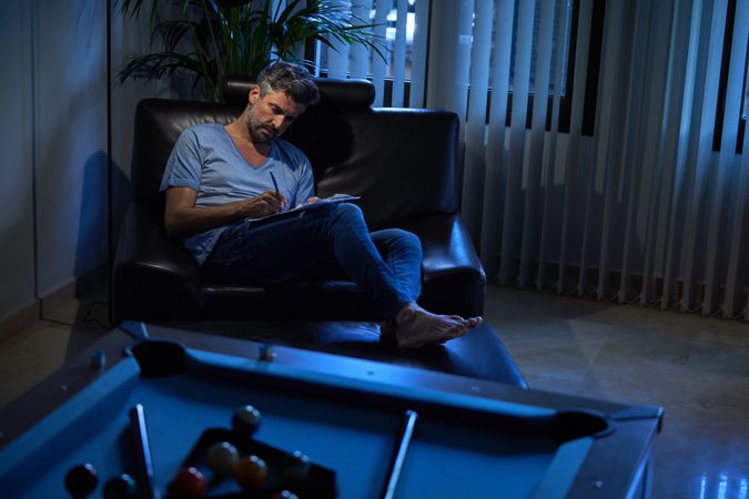 Businessman writing notes in armchair at dark workplace