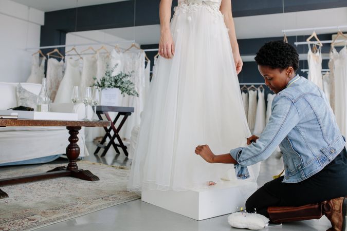 Female wedding dress designer making adjustment to bridal gown in her studio