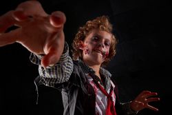 Boy disguised as a zombie with blood with his arms raised trying to catch something in front