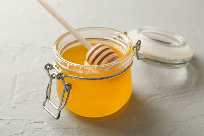 Glass jar with honey and dipper on neutral background, closeup