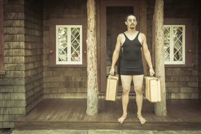 Gentleman Dressed in 1920’s Era Swimsuit Holding Suitcases on Porch