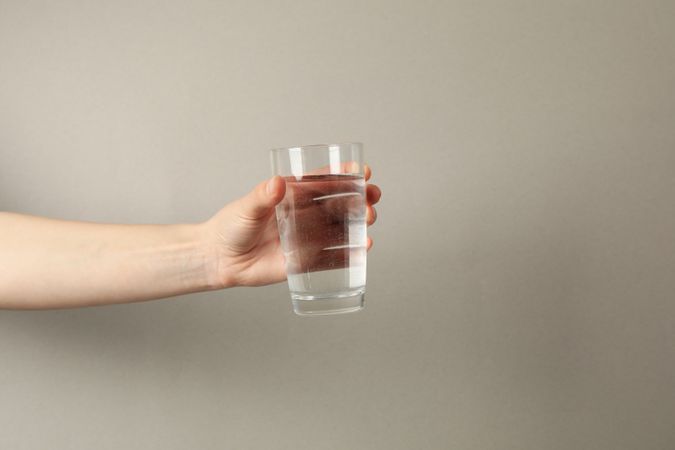 Hand holding full glass of water in beige room