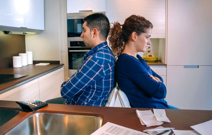 Couple with their backs to each other not talking in kitchen with bills on counter