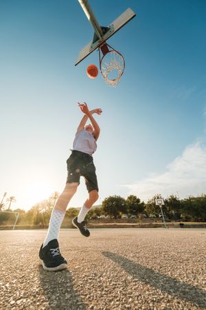 Boy throwing ball in hoop with hands raised