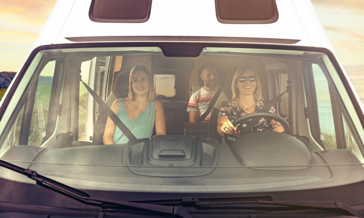 Three people smiling while driving in a motorhome