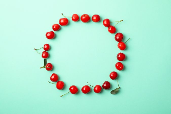 Circle made of red cherry on mint background, top view