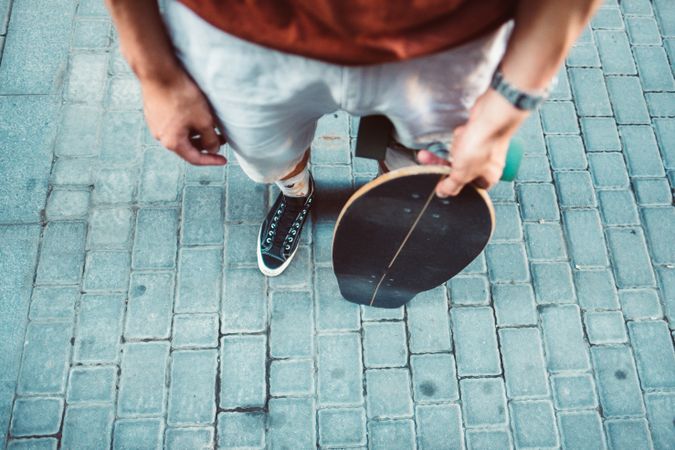 Sportive man carrying longboard while standing on street