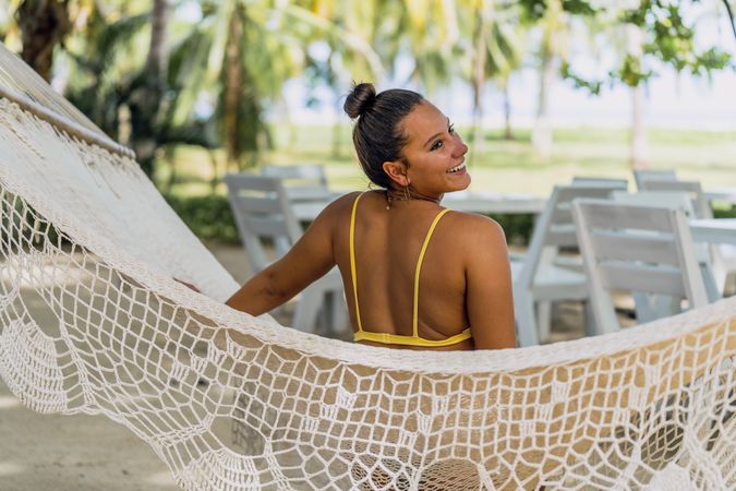 Joyful woman in bikini resting in hummock on beach
