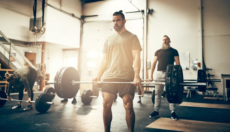 Serious man deadlifting in busy gym