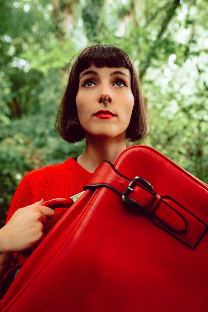 Woman in red with big red suitcase in forest