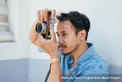Asian man in blue shirt with short dark hair holding camera 4mW9X0