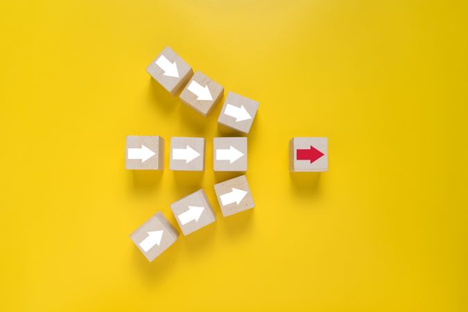 arrows and single red arrow pointing on wooden blocks isolated on yellow background. concept of leadership
