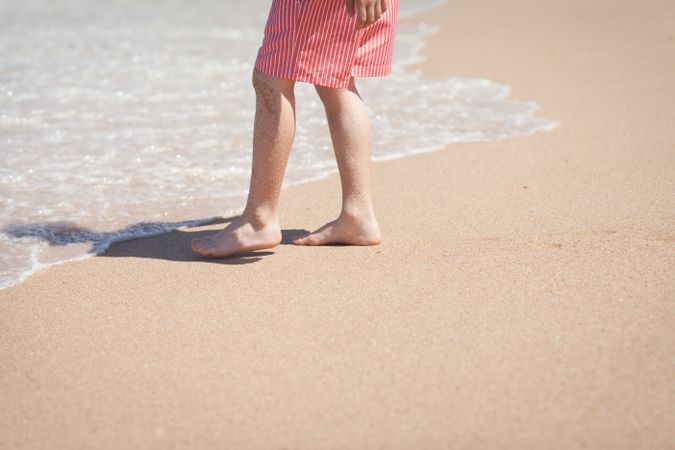 Crop legs near sea water on sand