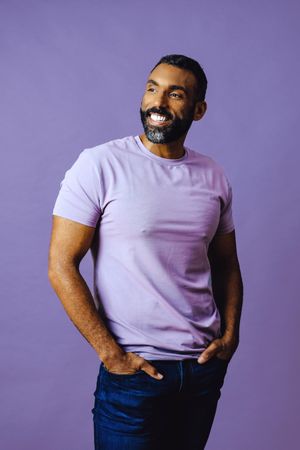 Smiling male in purple studio looking away with hands in pocket, vertical