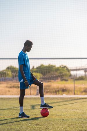 Black football player with ball standing on stadium