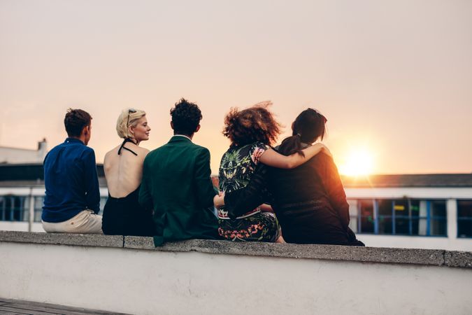 Rear view of young friends relaxing together on rooftop at sunset