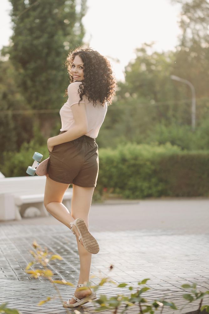 Back of smiling female teenager with skateboard in park with trees in background