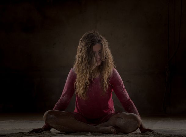 Young woman in lotus pose between sand in darkness