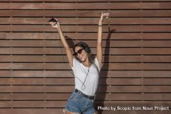 Young woman in light shirt and denim shorts listening to music with headphone and dancing outdoor 5oOX15