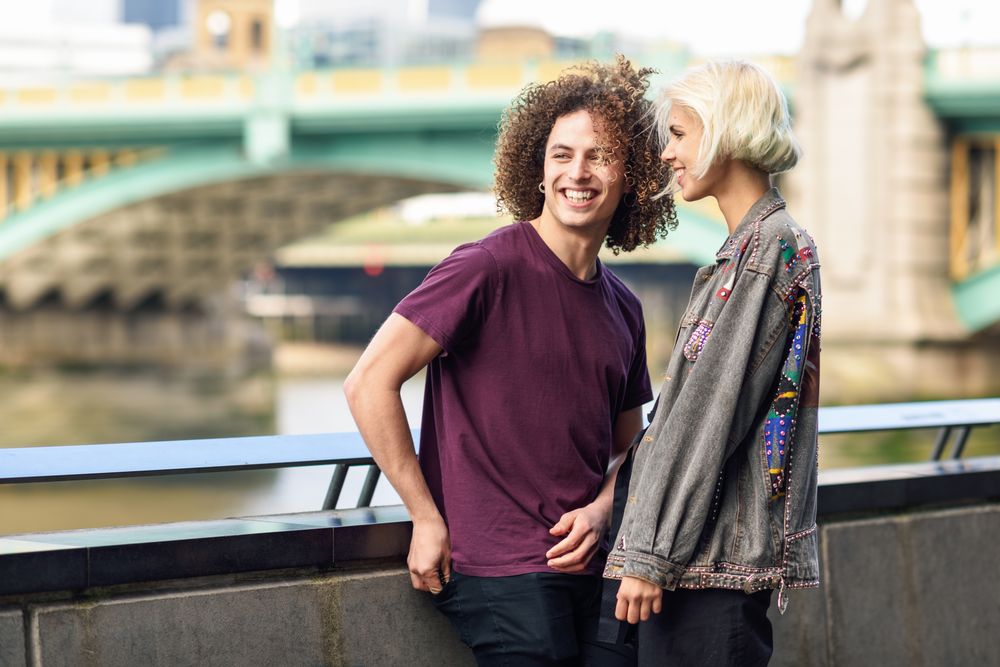 Man and woman laughing on riverwalk with bridge in background