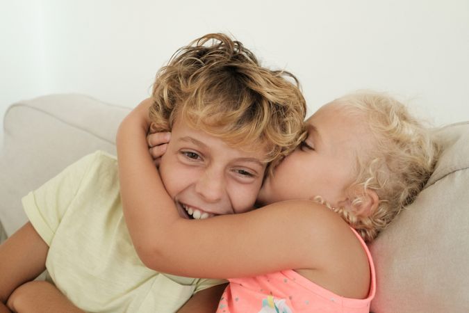 Loving sister kissing boy on sofa at home