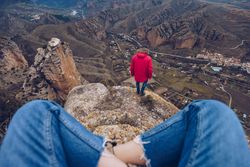 Person rest on cliff while tourist standing in edge and looking down