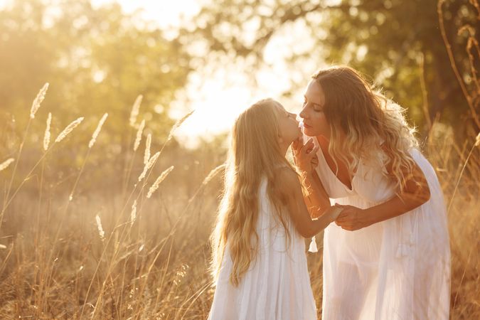 Woman going to kiss a little girls face in marsh at sunset