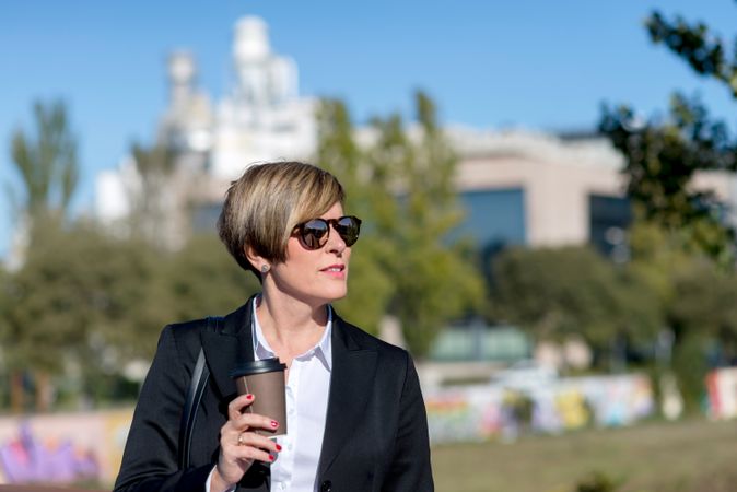 Woman holding coffee while walking around park