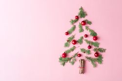 Christmas tree made with evergreen fir, bauble decoration and cinnamon sticks on pink background