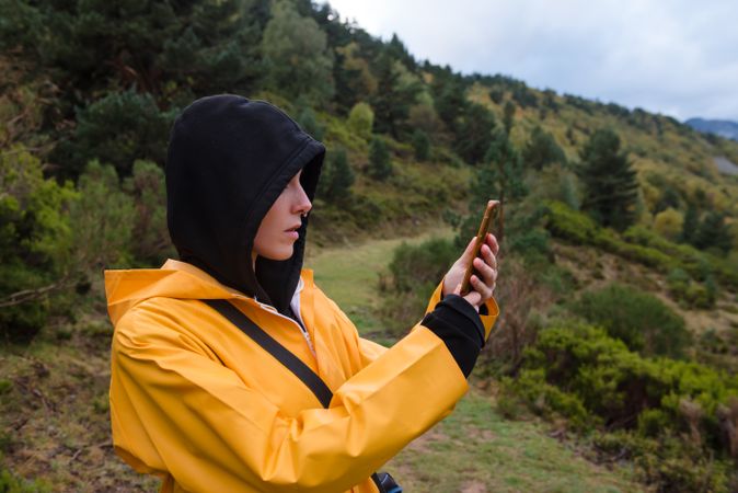 Woman in hoodie and yellow raincoat browsing smartphone