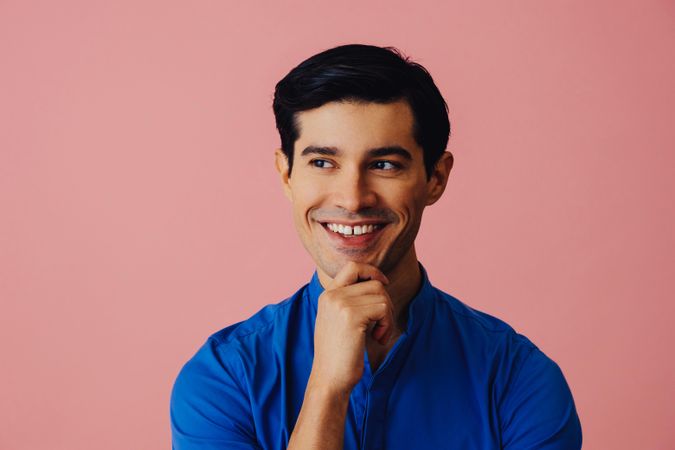 Latino man smiling in pink studio with hand on chin