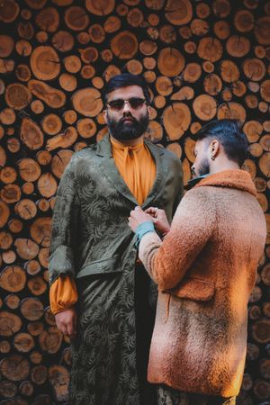Man closing the button of another man's coat beside tree logs
