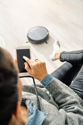 Female chilling on sofa with phone while robotic vacuum cleaner