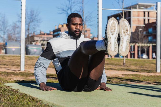 Determined Black sportsman working out with raised legs in city