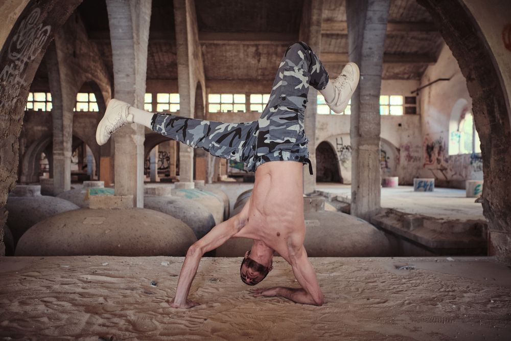 Muscular man performing cricket movement of breakdance in abandoned building
