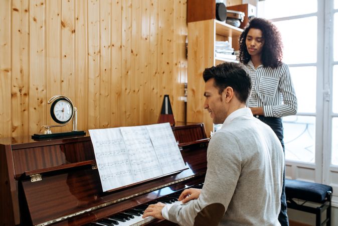 Man playing piano near woman teaching in studio