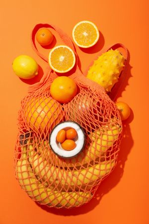Set of tropical fruit in bag on orange background, top view
