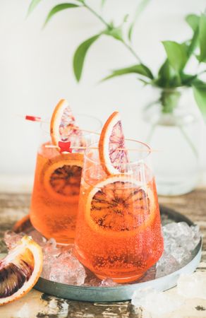 Two glasses of an orange cocktail with blood orange slices, eco straws and leaves in background