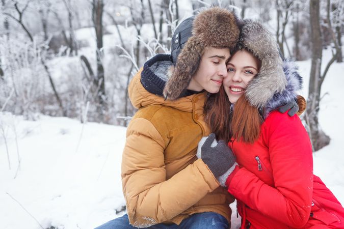 Loving teenage boy and girl sitting in snowy forest