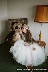 Young girl in light dress sitting on armchair holding bear plush toy 5n3384