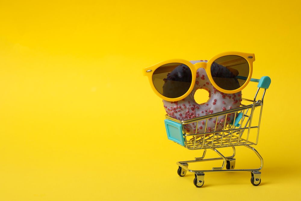 Shop trolley with sunglasses and donut on yellow background