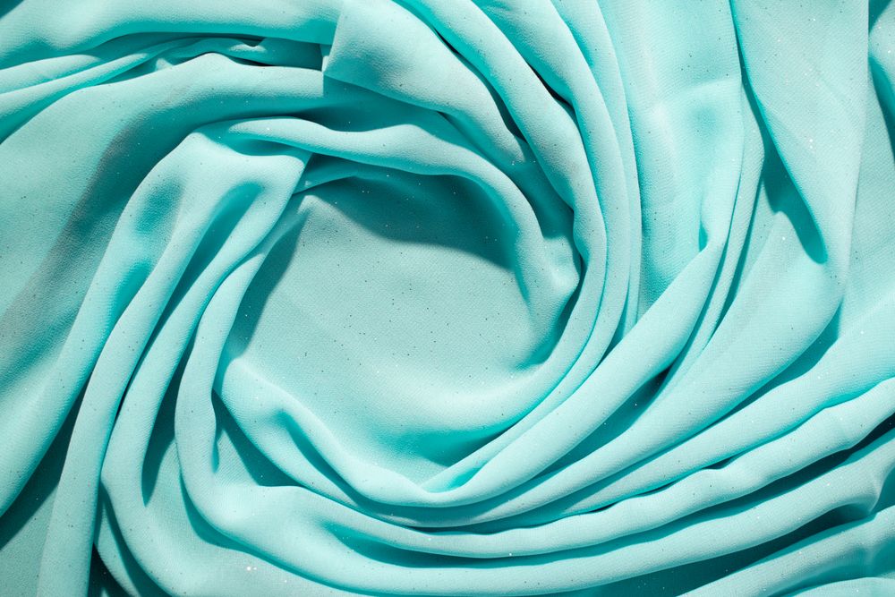 Spiral Twisted Turquoise wavy crumpled fabric with little sparkling dust and copy space in center, texture and  background.