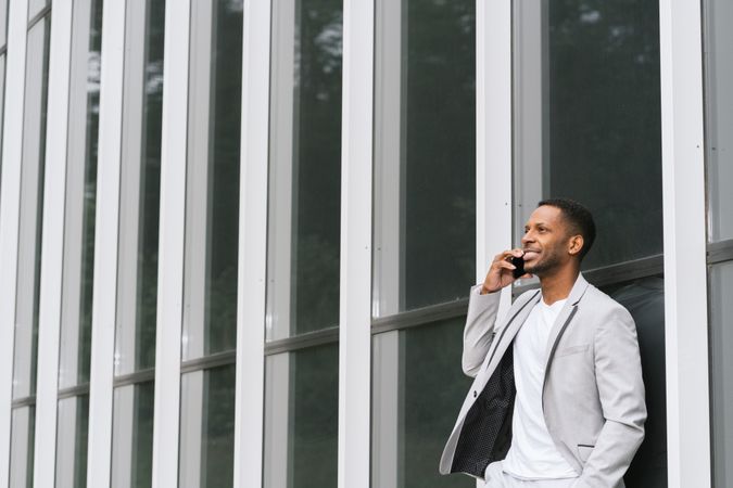 Elegant Black man talking smartphone leaning building