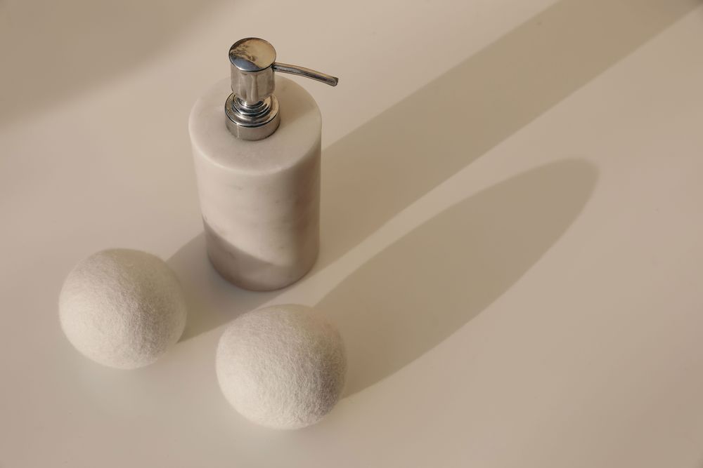 Dryer wool balls and luxury marble stone soap dispenser bottle on blurred beige table background in sunlight