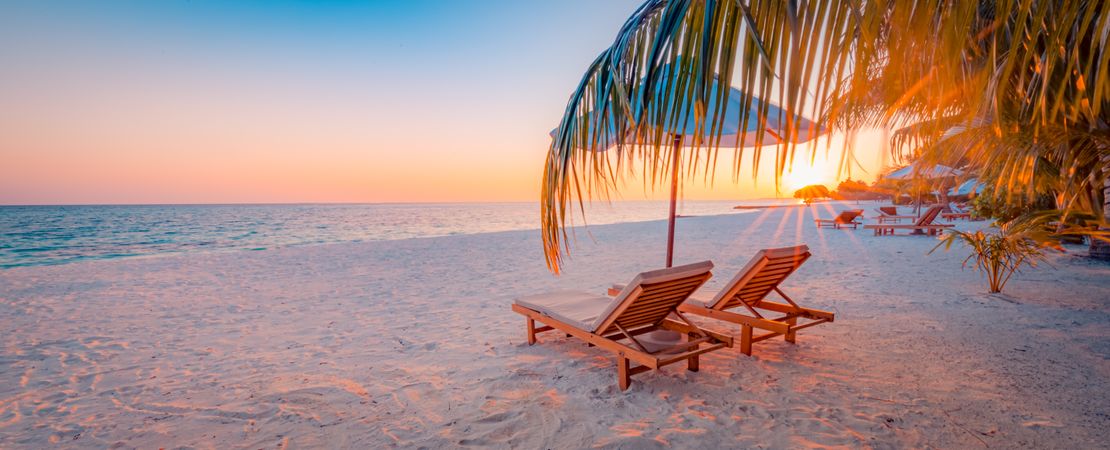 A tropical beach at sunset with reclining chairs