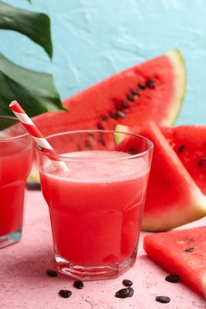 Composition with glass of watermelon juice and slices on pink table
