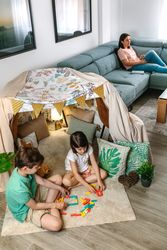 Children playing with stacking piece game while relaxed mother using remote control sitting on sofa