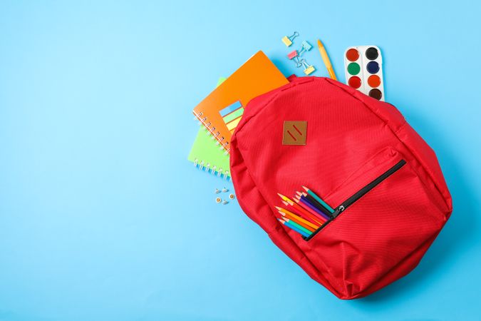 Flat lay composition with backpack and school supplies on color background